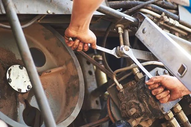 Hands using wrenches on heavy machinery engine components.