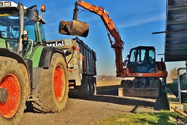 Excavator loading dirt into a large dump truck on a sunny day.