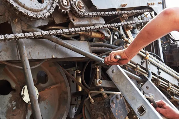 Mechanic adjusting machinery components using a wrench on heavy farm equipment.